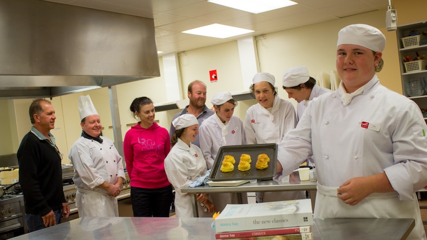 Glossop High School student Zoe Harrington stands with a tray of pastries in front of fellow students and staff.