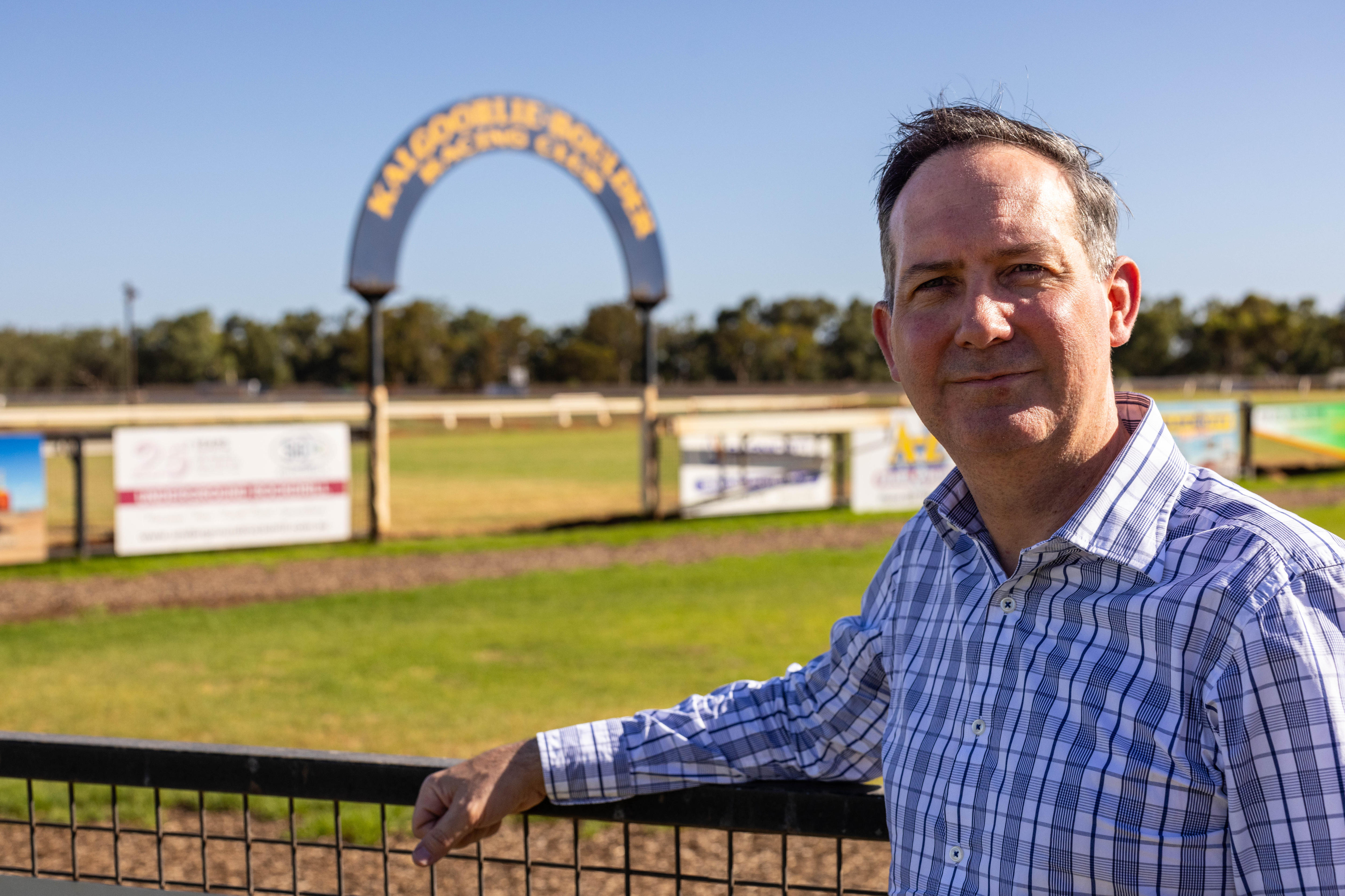 Un hombre con una camisa de negocios apoyado en una valla en una pista de carreras.  