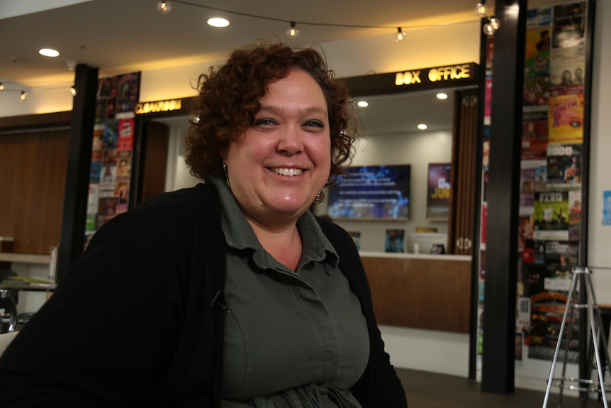 A woman sits in a chair in a theatre hall, smiling.