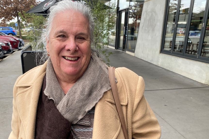 A woman wearing a jacket and scarf smiles.