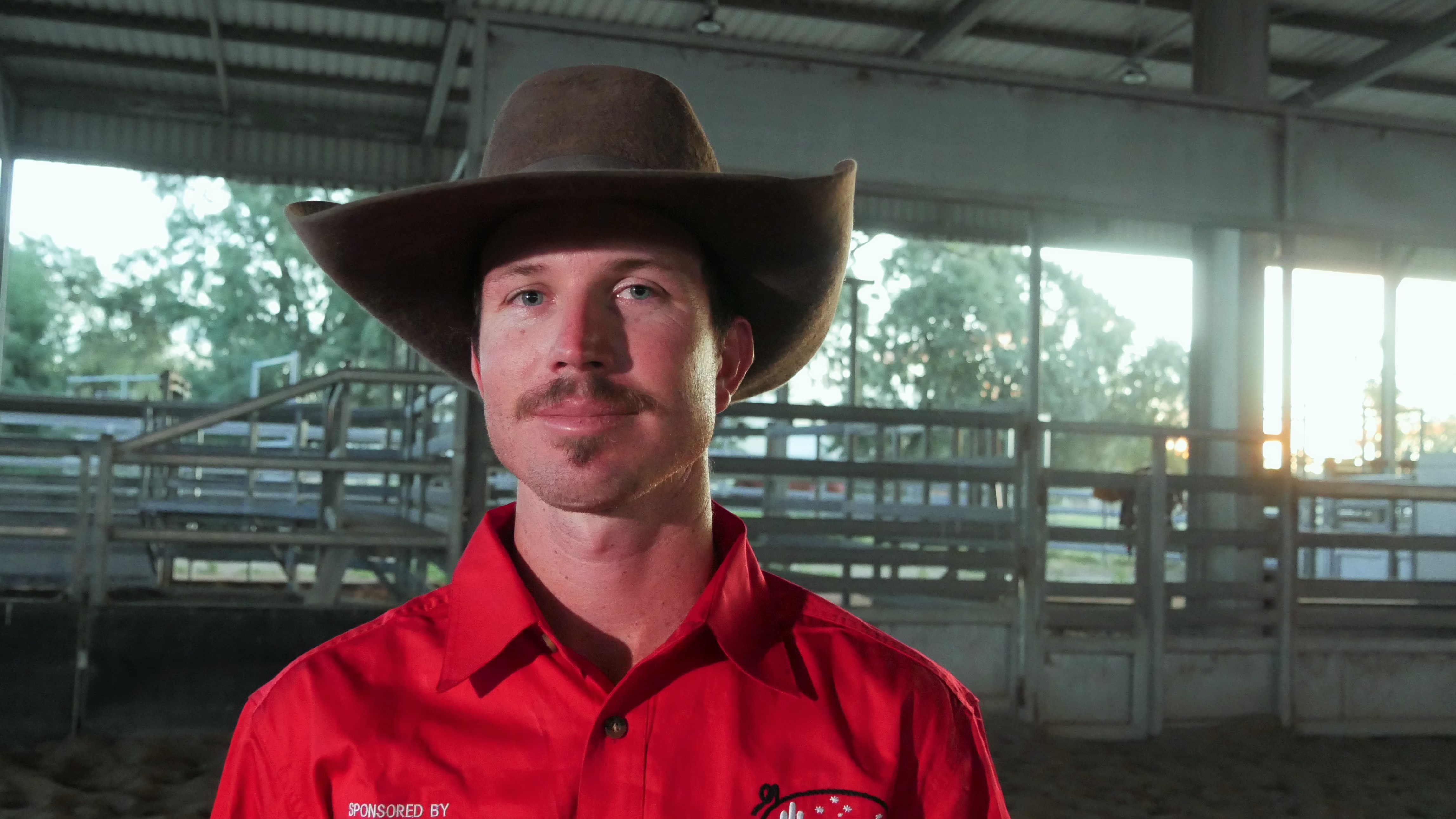 A man in a red shirt, with a mustache and a large hat.