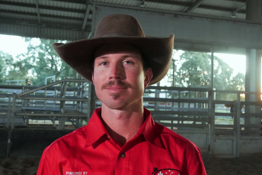 A man in a red shirt, with a mustache and large hat.
