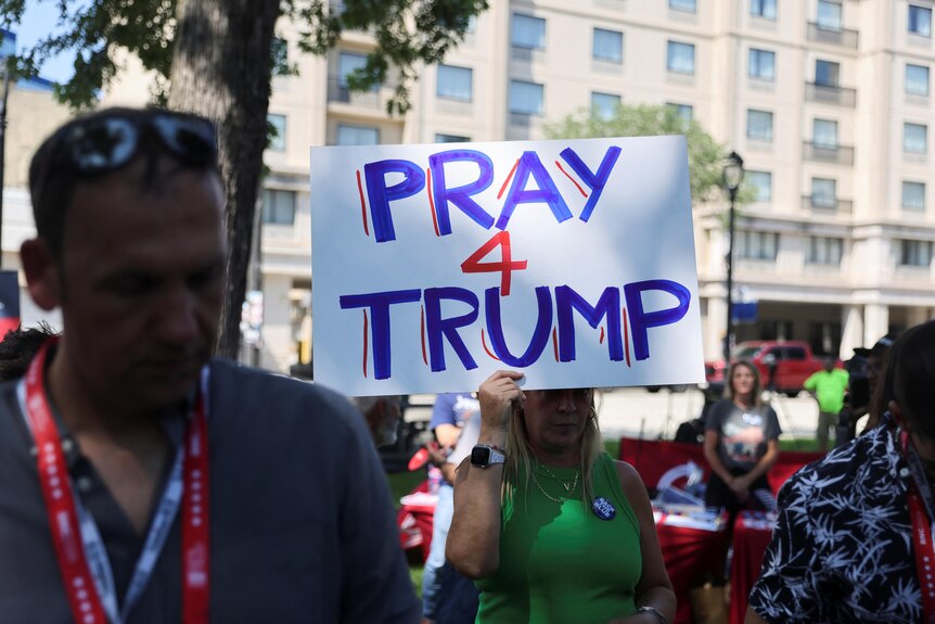 A woman holds a sign that says Pray 4 Trump.
