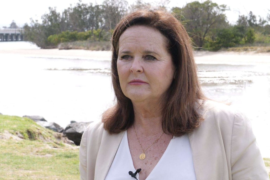 A woman with shoulder-length brown hair stands in front of a lake.