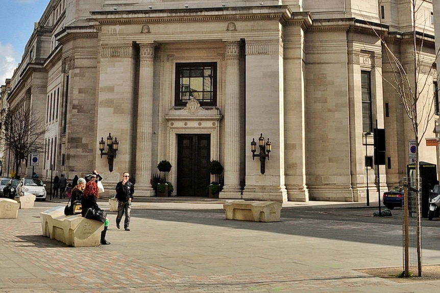 Two women sit on an uncomfortable looking concrete bench outside Freemasons' Hall in Camden, UK.