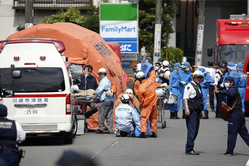 Rescue workers and police officers on a blocked road treat people injured in a stabbing attack