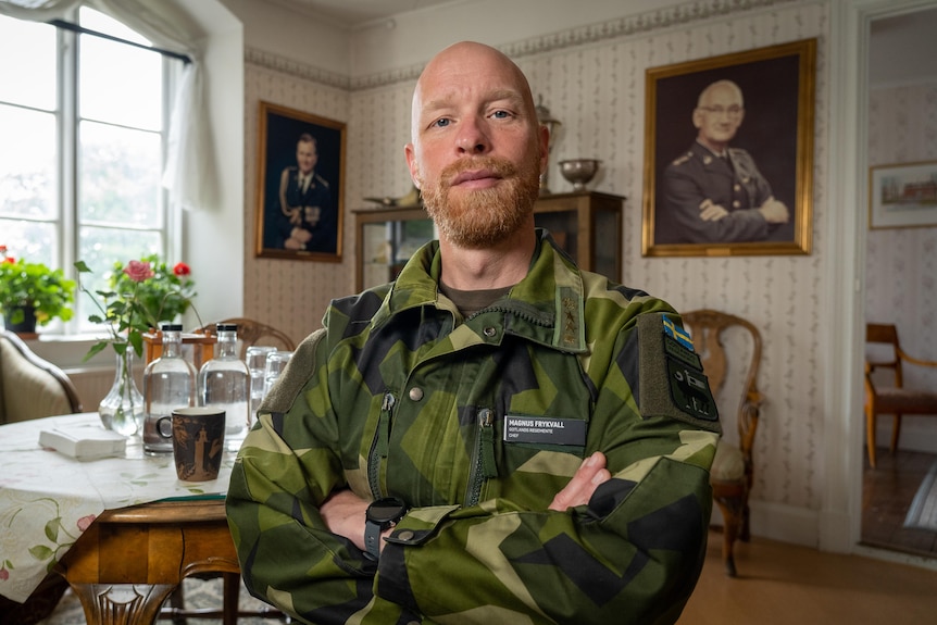 A man in military fatigue poses with his arms crossed.