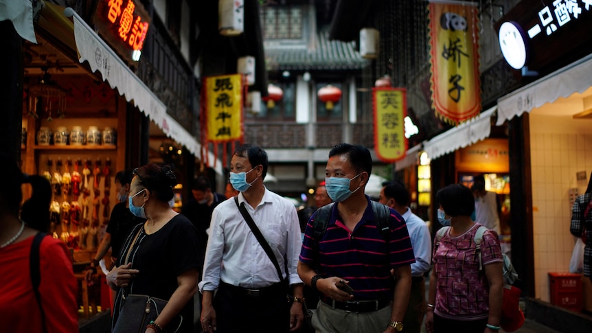 People wearing masks walk through a Chinese street.