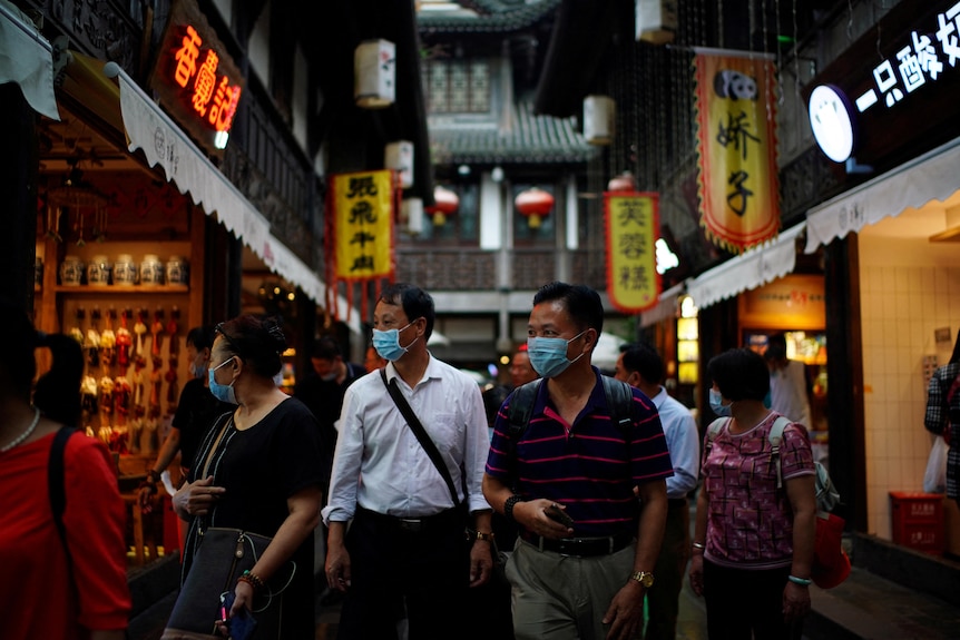 People wearing masks walk through a Chinese street.