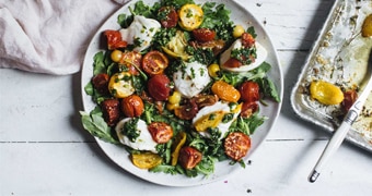 A plate of caprese salad with a bed of baby rocket, topped with roasted tomatoes, mozzarella cheese, thyme and basil oil.