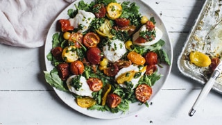 A plate of caprese salad with a bed of baby rocket, topped with roasted tomatoes, mozzarella cheese, thyme and basil oil.