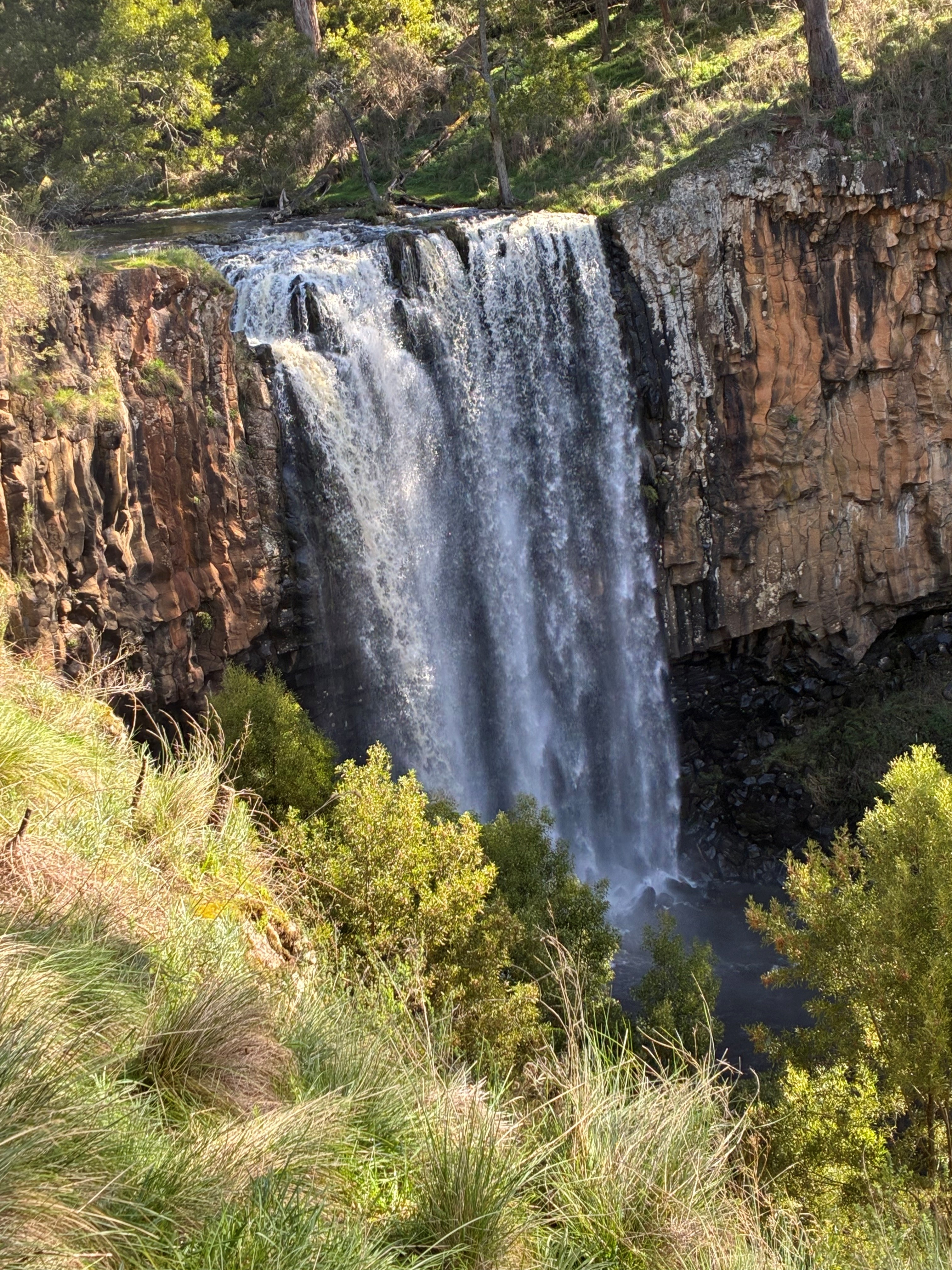 A tall waterfall splashing over a cliff into a waterhole.