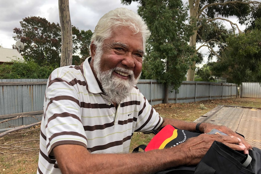 A smiling man with a beard sits at an outdoor table.