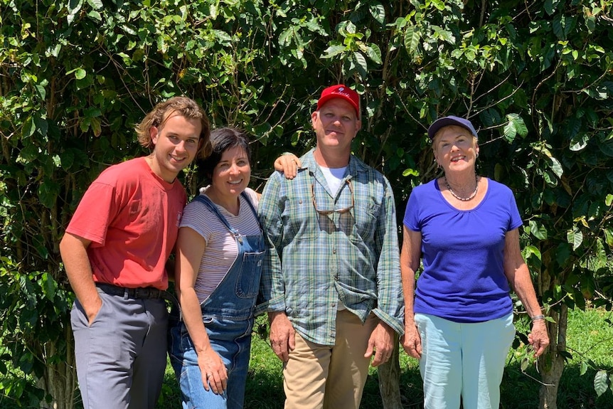 A family dressed in bright colours stand together smiling in front of a hedge.