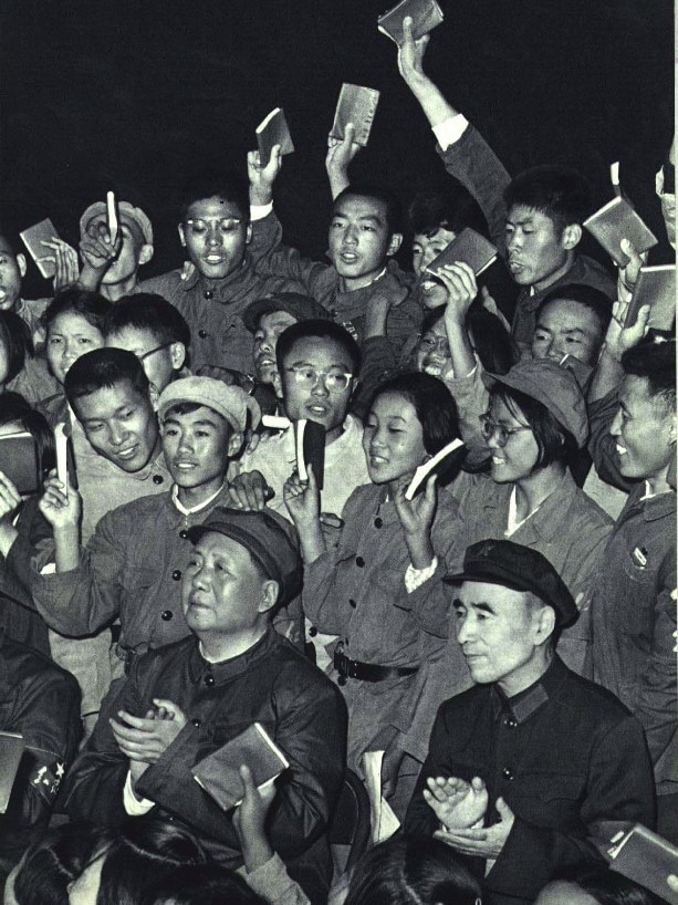 A portrait black and white image shows a crowd of young people in similar military-style suits.