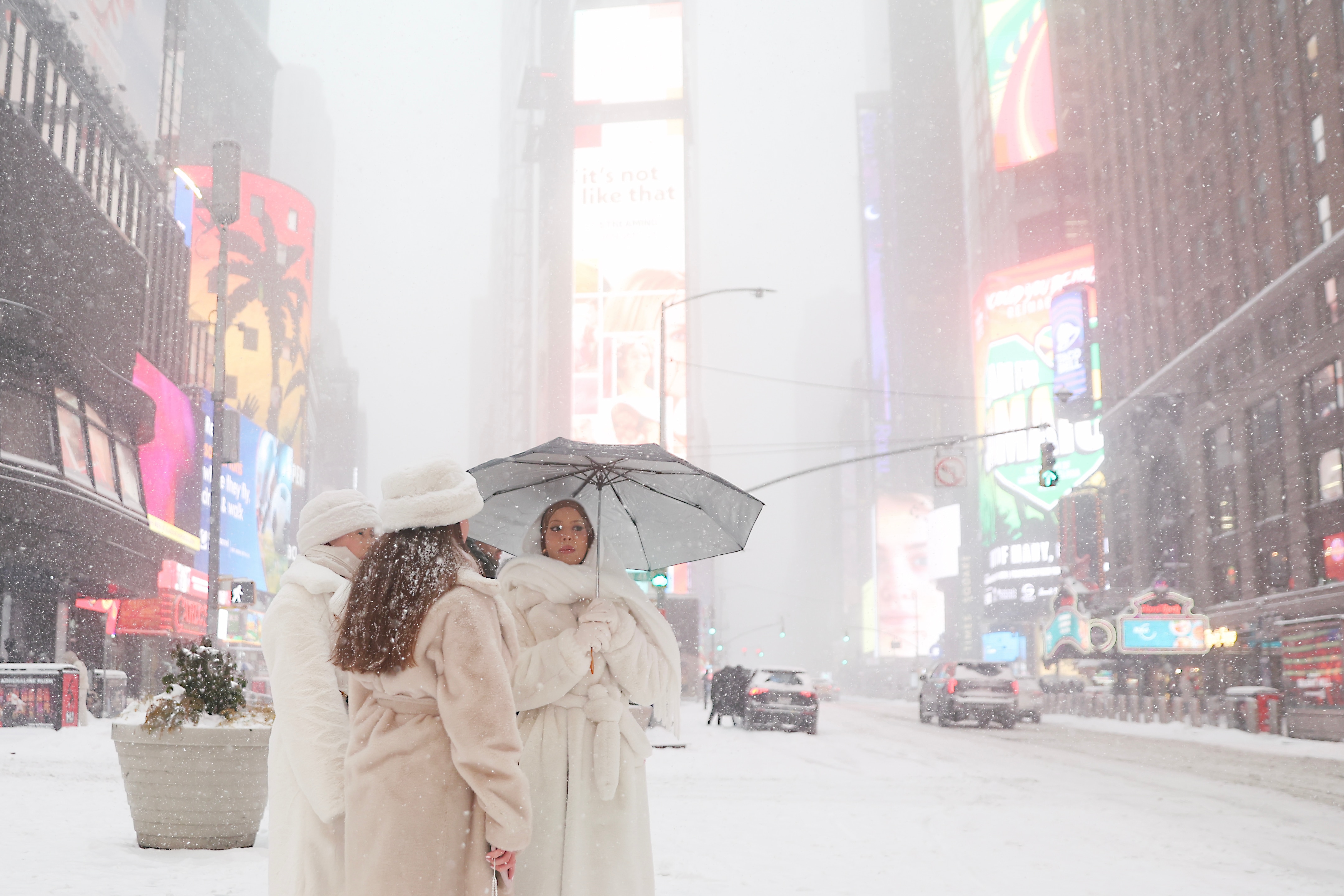 Las mujeres visten abrigos de piel blancos y sombreros en un Times Square nevado en Nueva York.