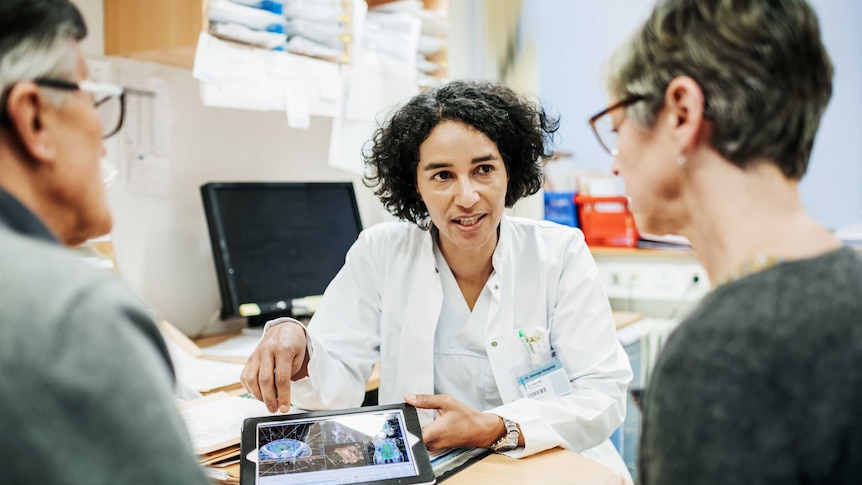 A clinical doctor explaining a medical procedure to an elderly couple.