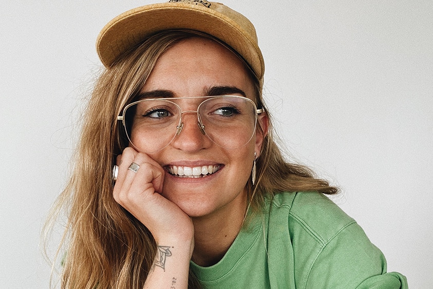 A young woman in glasses wearing a baseball cap.