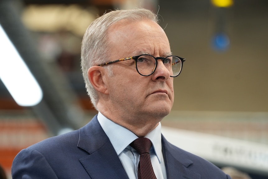 A man in glasses and a suit with a stern expression on his face