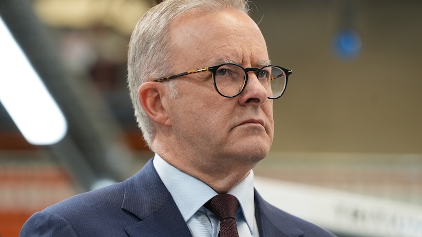 A man in glasses and a suit with a stern expression on his face