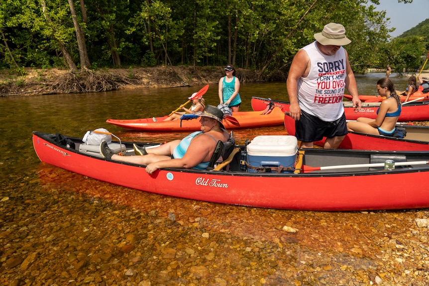 People lounge in canoes lined up on a river bank 