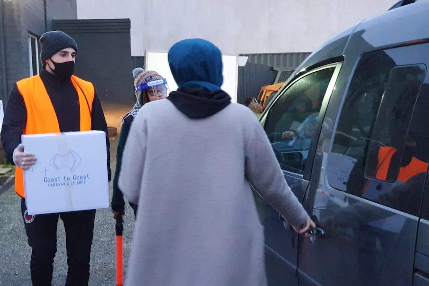 A man carryting a box and walking to a parked car