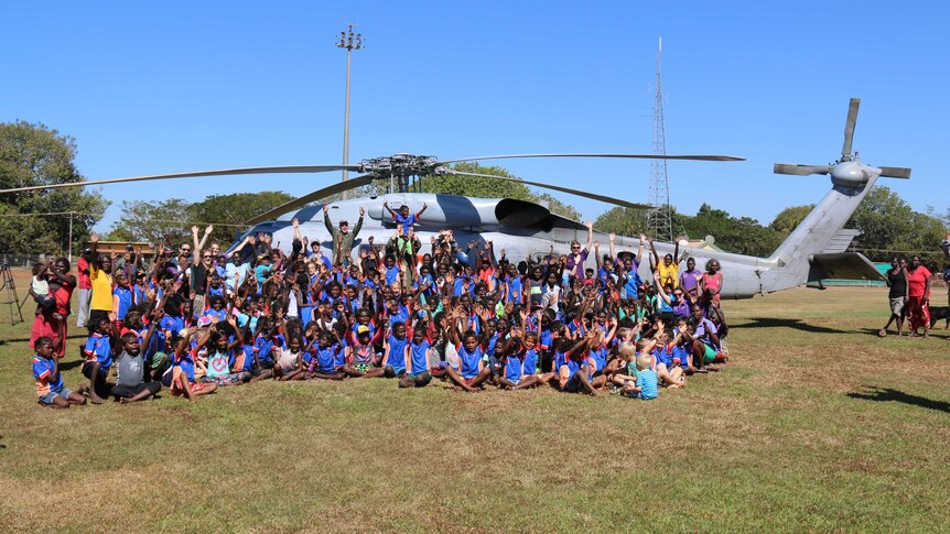 A group of Tiwi Islands school students waves to the camera with Navy officers
