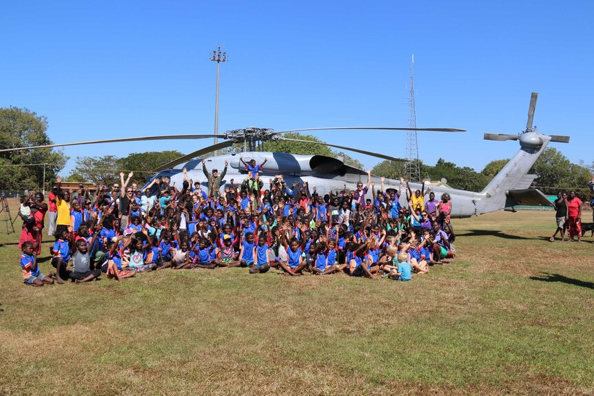 A group of Tiwi Islands school students waves to the camera with Navy officers