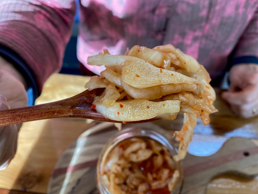 kimchi held up on a wooden spoon above a glass of kimchi