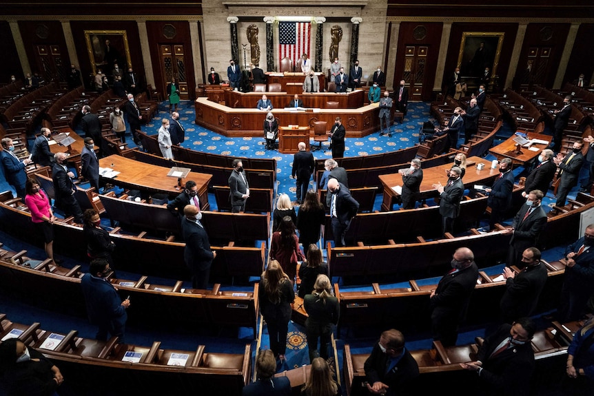 An overhead shot shows the House of Representatives Chamber, a handful of politicians milling about inside