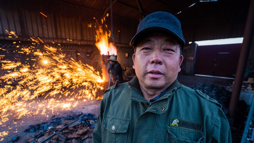 A man poses for the camera while molten iron is flung behind him