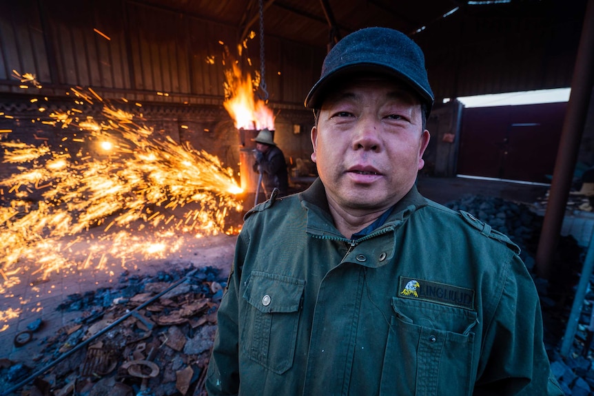 A man poses for the camera while molten iron is flung behind him