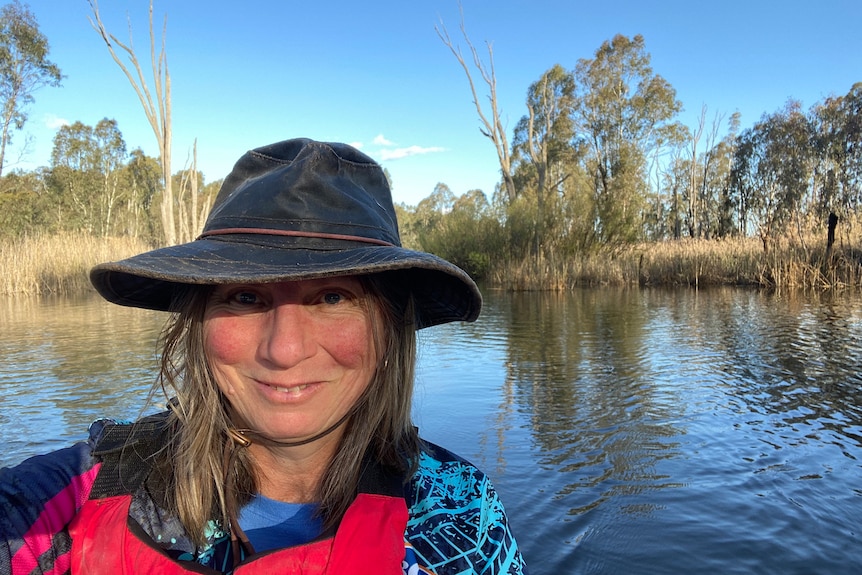 A woman with a blue hat in a kayak smiles at the camera 