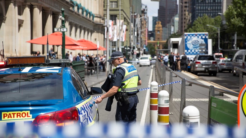 A police officer stands in front of a line of tape, closing Elizabeth Street near the corner of Bourke Street.
