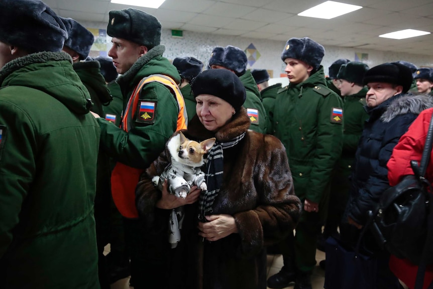 Wide shot of a group of uniformed soldiers and a woman carrying a dog.