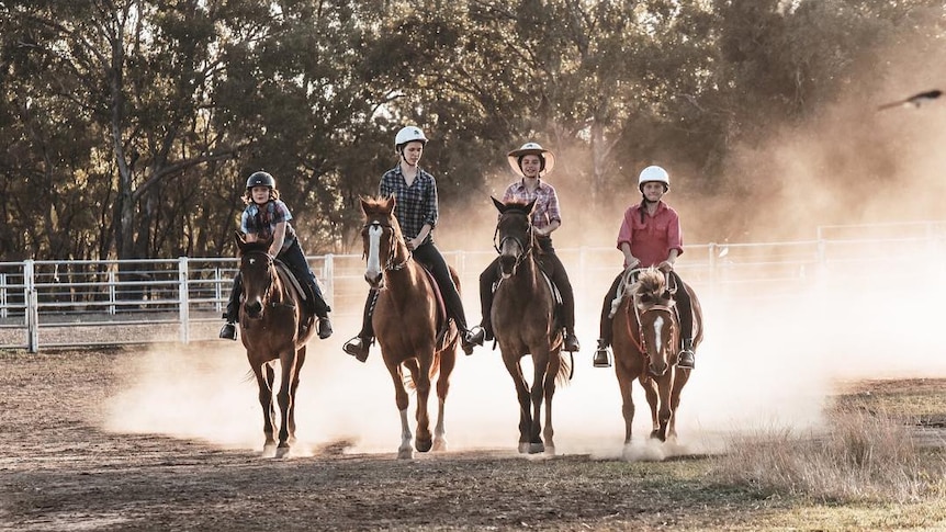 Four friends ride their horses along a dusty road.