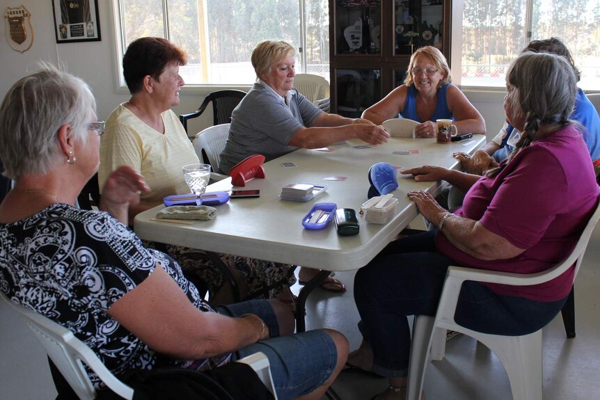 A group of CMCA members play cards on a long table.