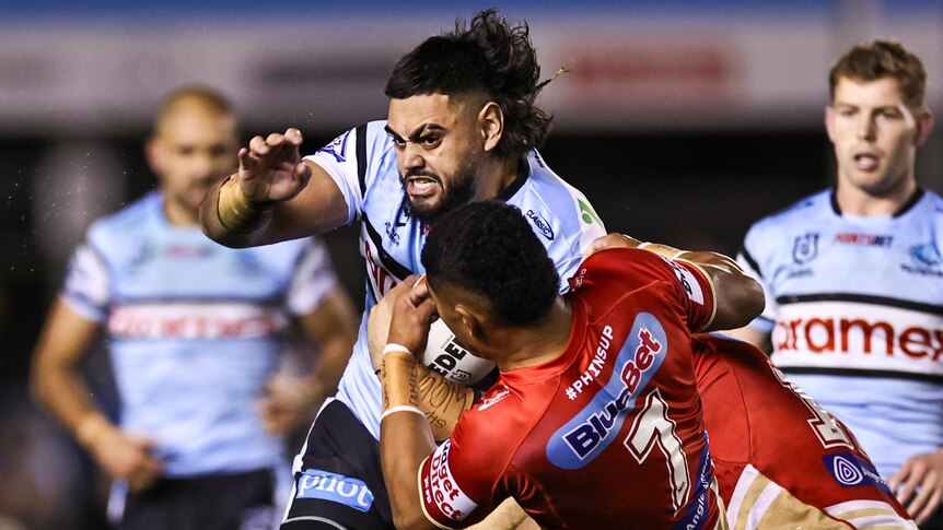 NRL player Royce Hunt of the Sharks breaks through the defence of Isaiya Katoa, while being tackled by another