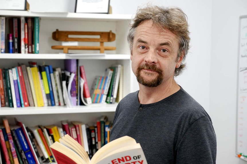 Psychologist Paul Duckett stands in front of a bookcase while reading a book