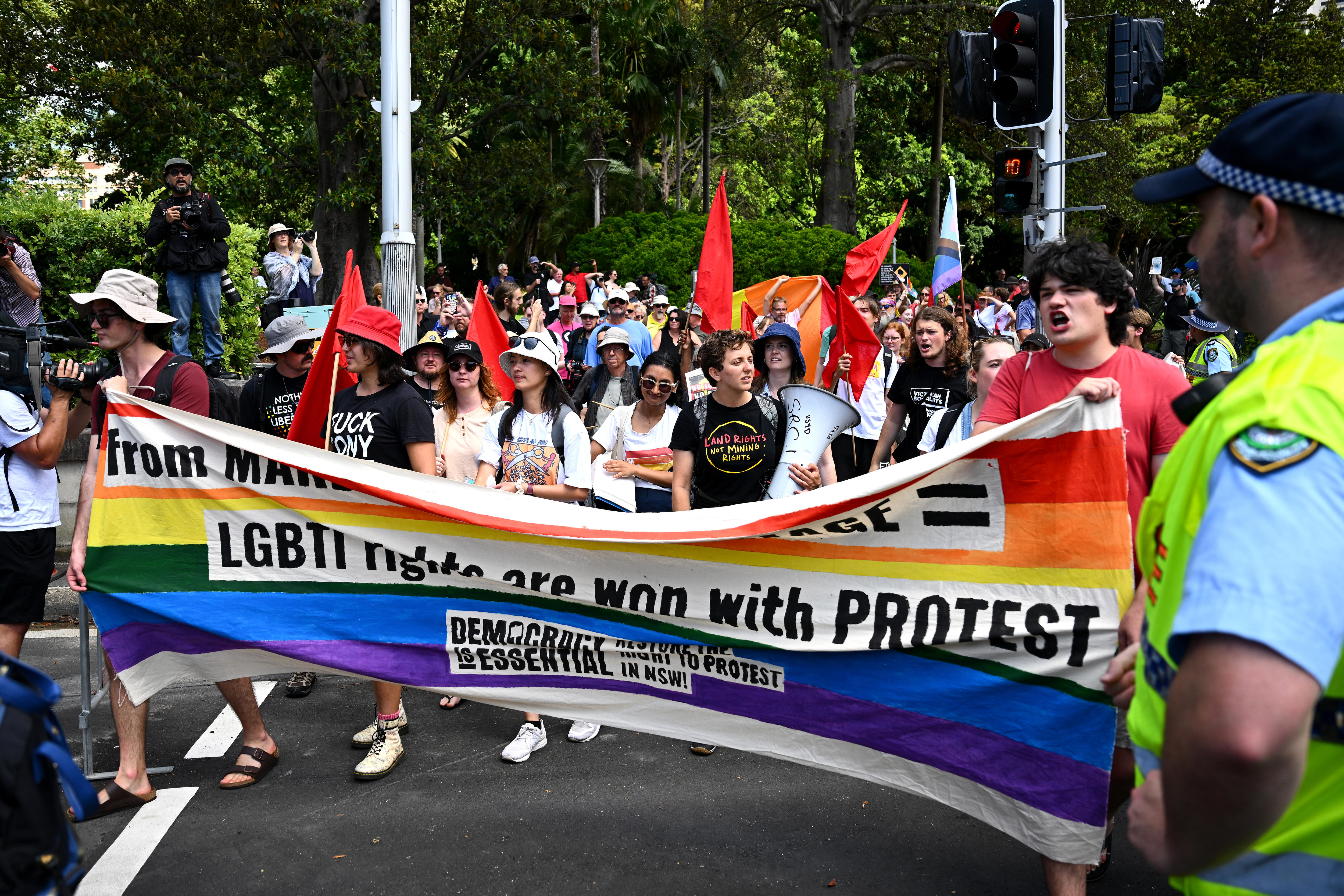 Large crowd holding rainbow flag with LGBT protest slogans 