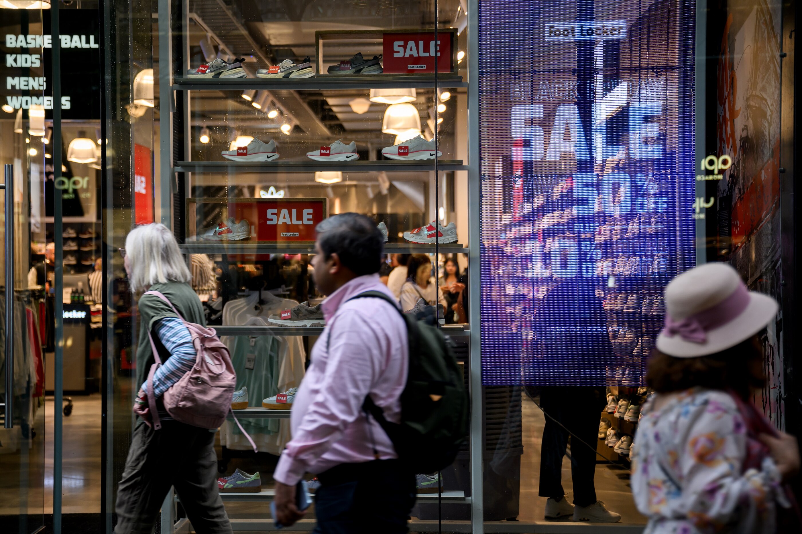 A small crowd of people walk past a store that's advertising a sale.
