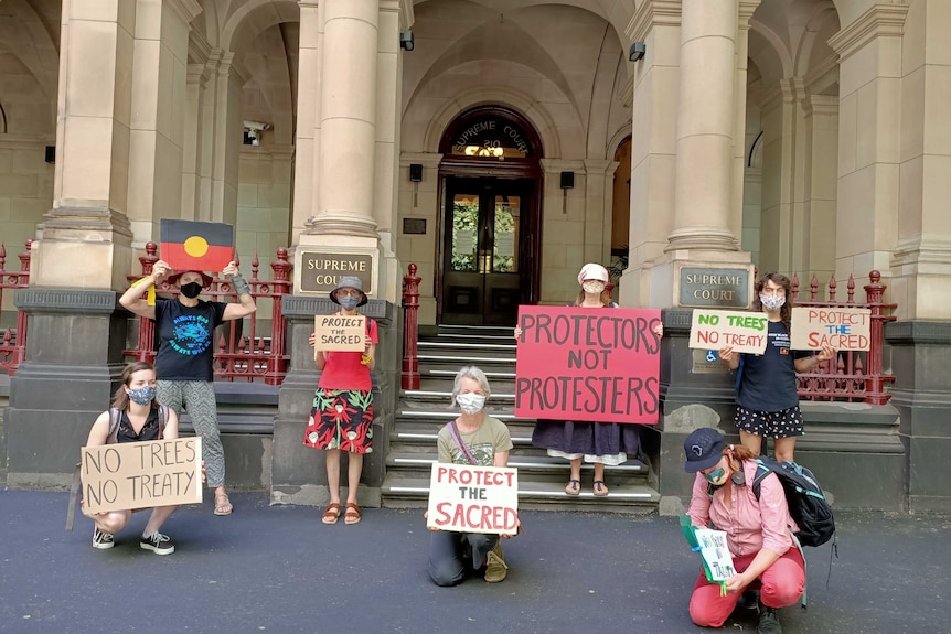 Six protesters in face masks stand outside the supreme court in Melbourne with signs protesting the western highway project