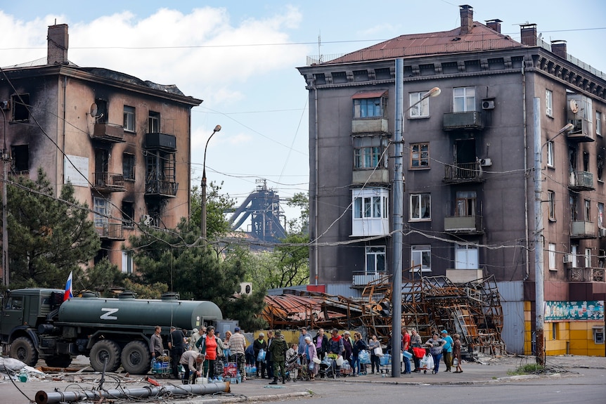 Civilians gather to receive clean water distributed by a Russian military tanke with the letter Z painted on it.