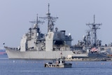 A small vessel patrols waters near a moored large grey US guided missile cruiser.