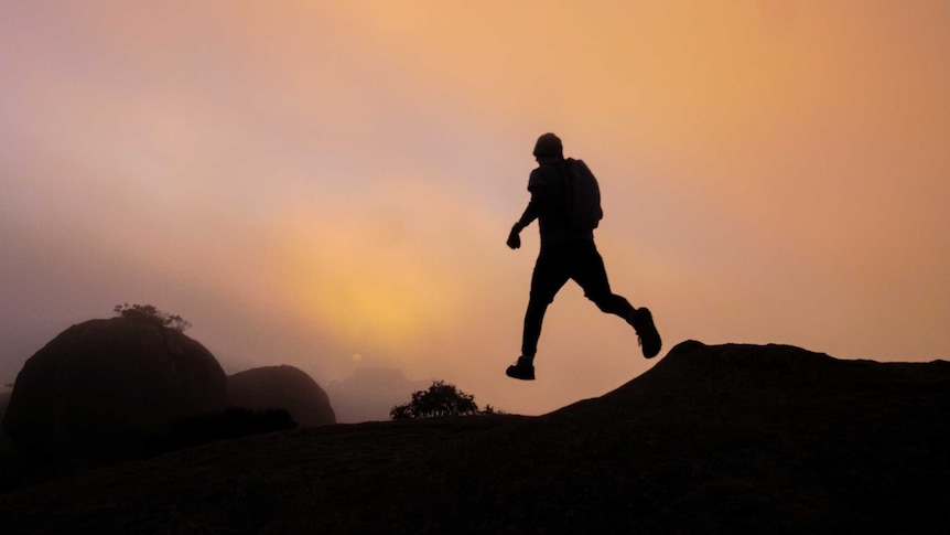 A runner is silhouetted by a crimson sunrise as he heads down the trail