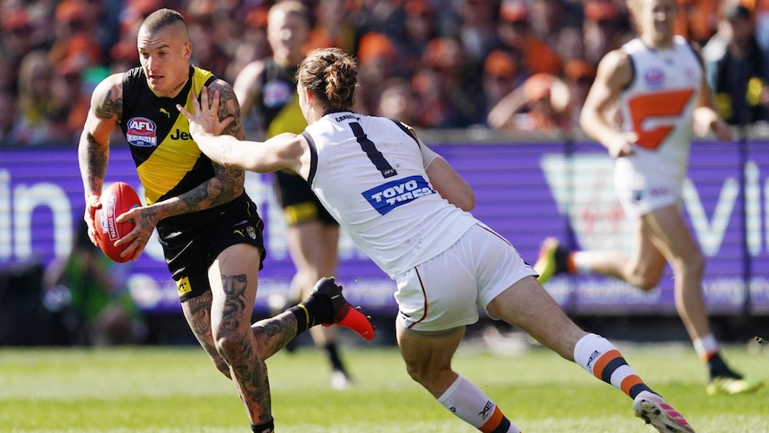 An AFL player charges with the ball as a defender makes a failed attempt to tackle him.