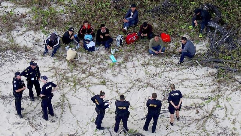 Police officers stand around group of people, allegedly illegal arrivals, sitting on a beach in far north Queensland.