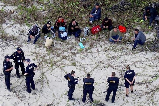 Police officers stand around group of people, allegedly illegal arrivals, sitting on a beach in far north Queensland.