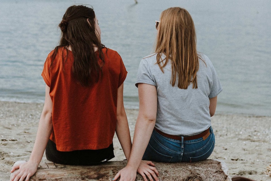 Two young women sit on the beach facing the ocean for a story about helping someone out of an abusive relationship.