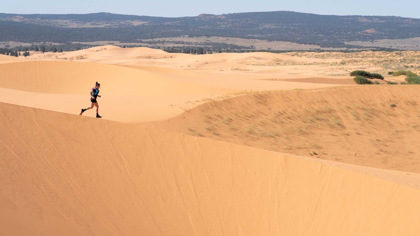 An athlete runs through sand dunes in the Grand Canyon region of the USA.